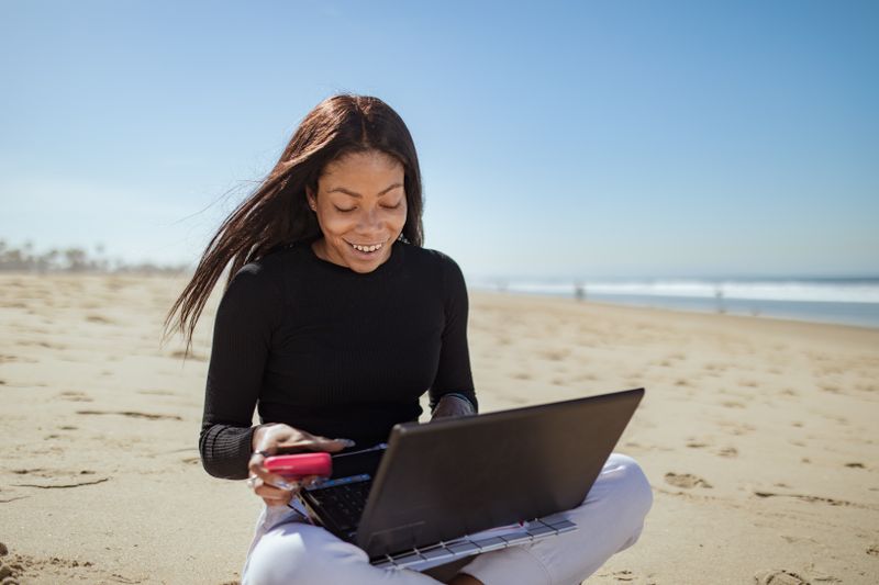 A woman smiling as she works on her laptop on a sunny beach